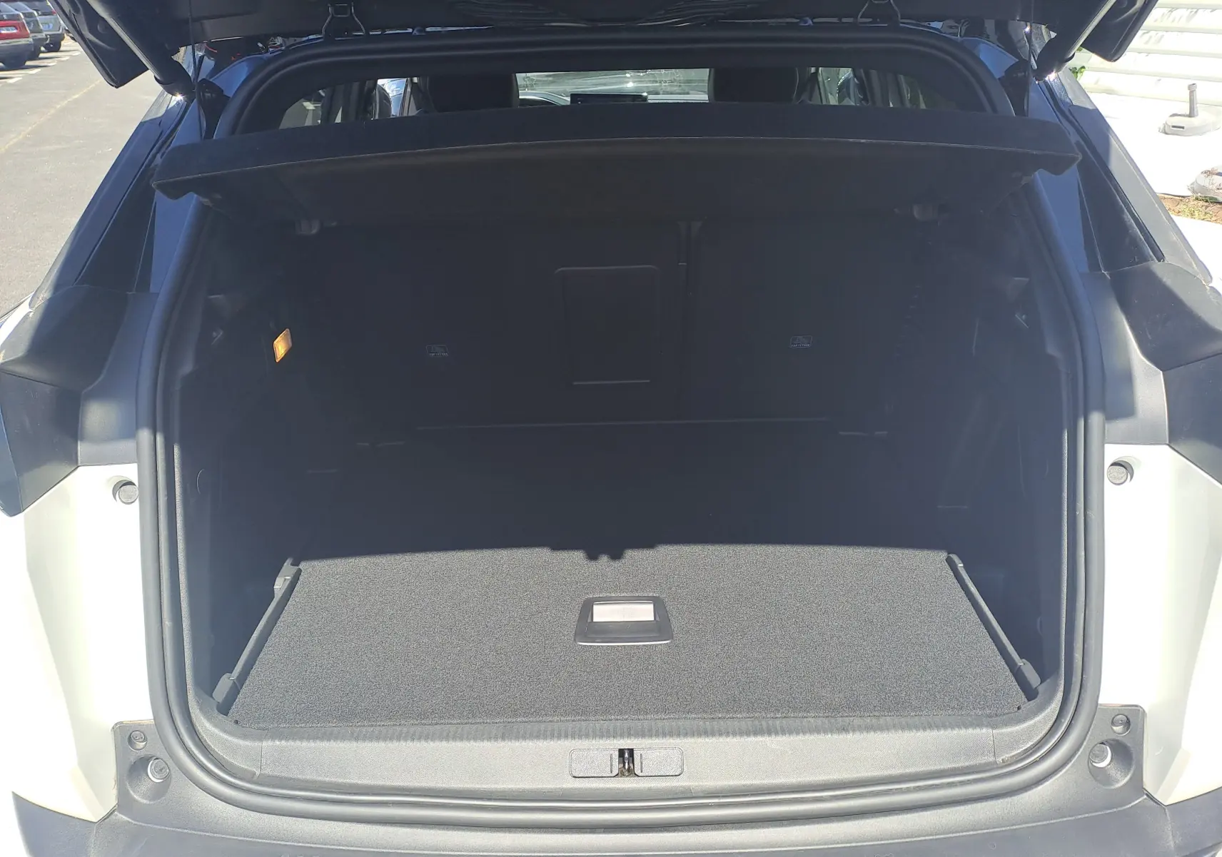 Coffre ouvert vu de l'arrière d'un Peugeot 3008 blanc nacré avec toit noir, montrant un espace de chargement vide.