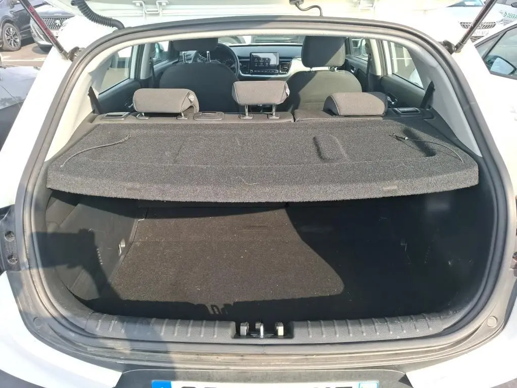 Coffre ouvert vu de l'arrière d'un KIA STONIC blanc 2023, avec cache-bagages et sièges arrière visibles.