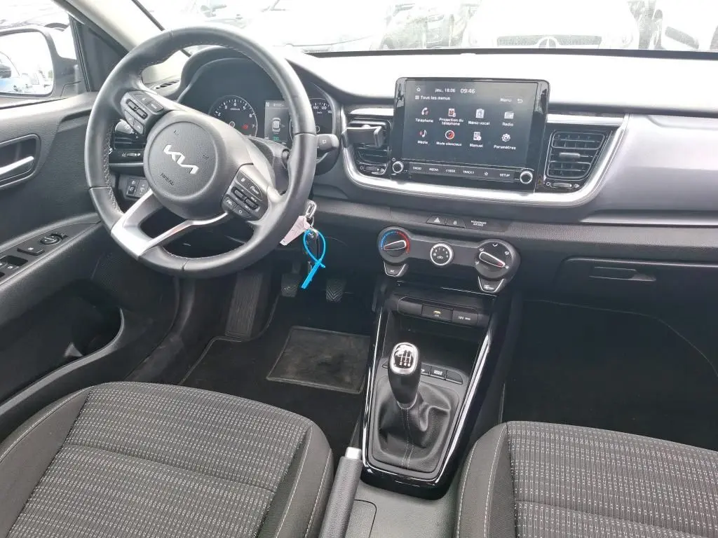 Vue intérieure côté conducteur du Kia Stonic blanc 2023, avec volant multifonction, écran tactile et boîte manuelle.