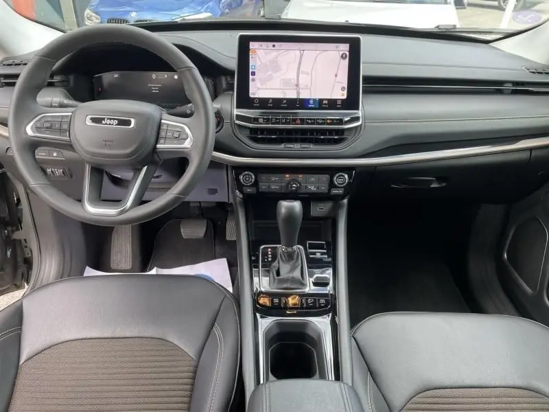 Vue intérieure avant du Jeep Compass 2023 gris, montrant le tableau de bord avec écran tactile central et volant multifonction.
