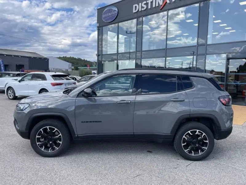 Vue de profil côté gauche d'un Jeep Compass gris hybride rechargeable 2023 devant un bâtiment vitré.