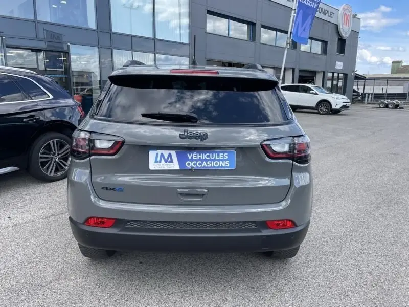 Vue arrière d'un Jeep Compass gris 2023 hybride rechargeable avec badge 4Xe, stationné devant un concessionnaire.