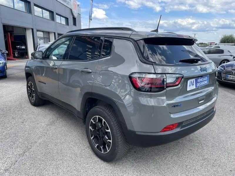 Vue 3/4 arrière droite d'un Jeep Compass gris 2023 hybride rechargeable avec jantes noires et vitres teintées.