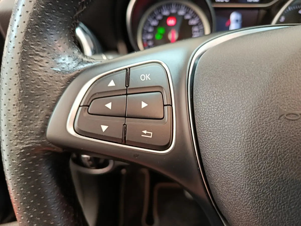 Gros plan sur les commandes gauche du volant cuir noir du Mercedes GLA 220 d Business Exec 2018, tableau de bord en arrière-plan.