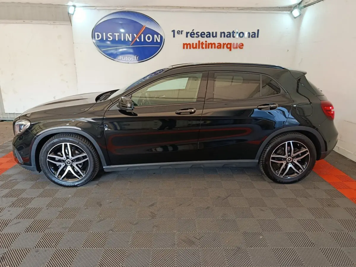 Profil côté gauche d'un Mercedes GLA 220 d noir 2018 avec jantes alliage et vitres teintées en intérieur showroom.