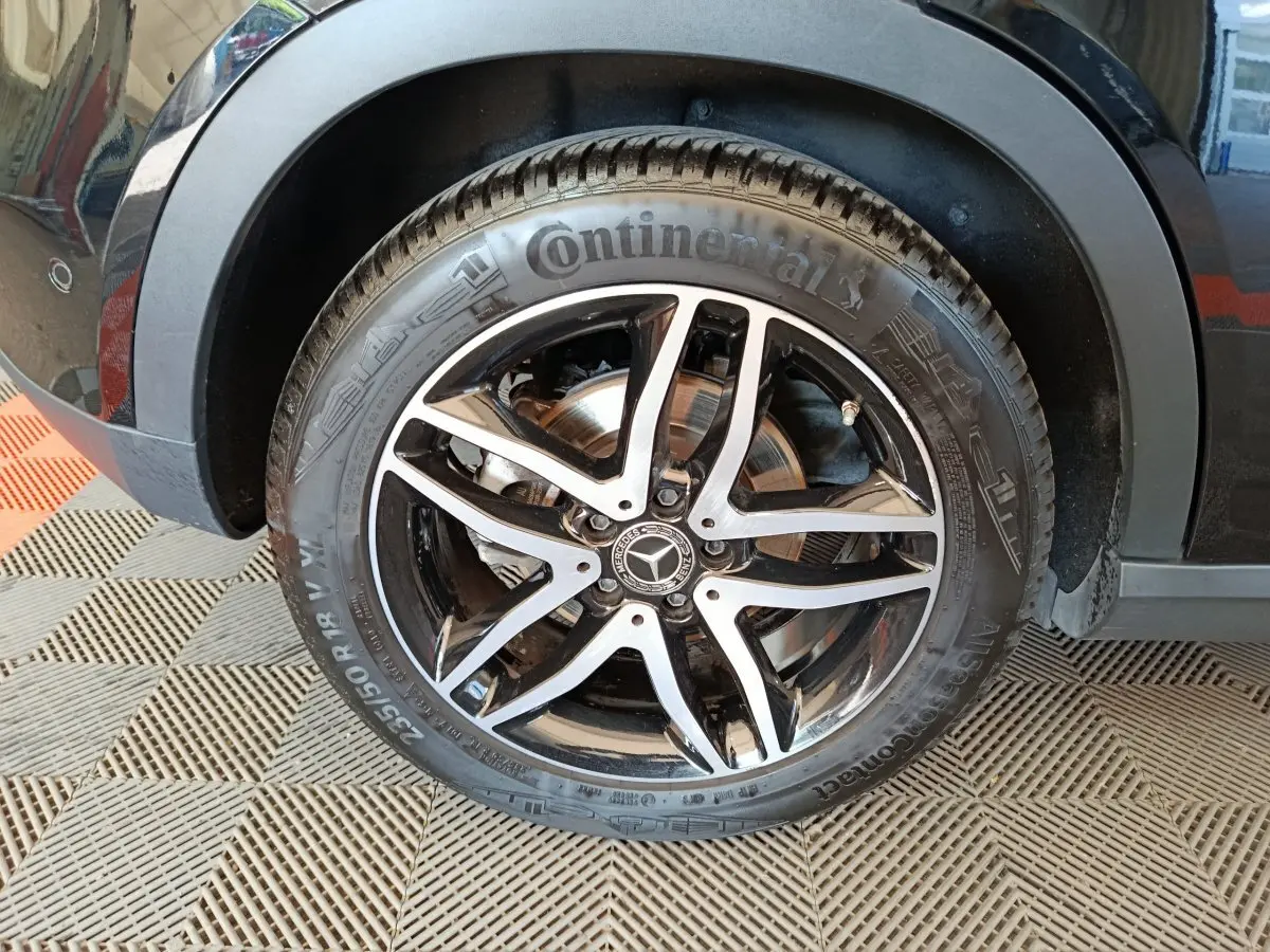 Gros plan sur la roue avant gauche noire d’un Mercedes GLA 220 d avec jante alliage cinq branches bicolore.