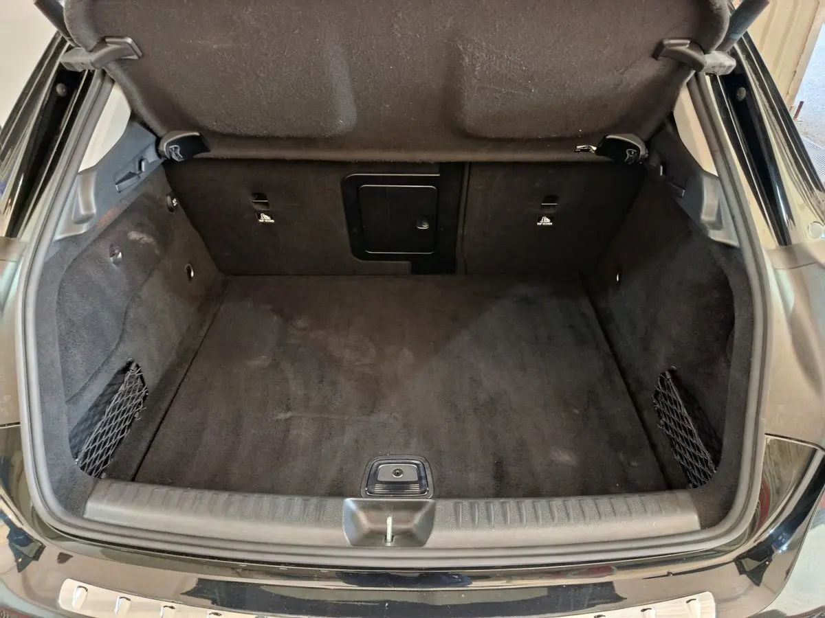Coffre ouvert vu de l'arrière d'une Mercedes GLA 220 d Business Exec noir, tapis et parois intérieures en tissu noir.