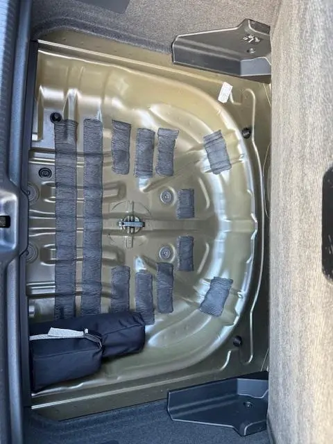 Coffre ouvert vu de dessus d’un Audi Q2 noir 2023, montrant la partie métallique sous la tablette arrière sans roue de secours.