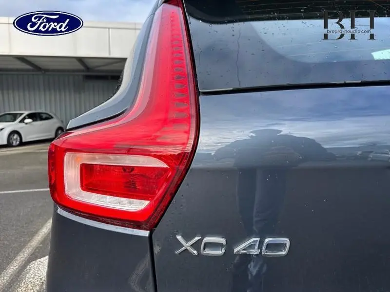 Gros plan sur le feu arrière gauche et le logo XC40 d’un Volvo bleu Denim sous la pluie.