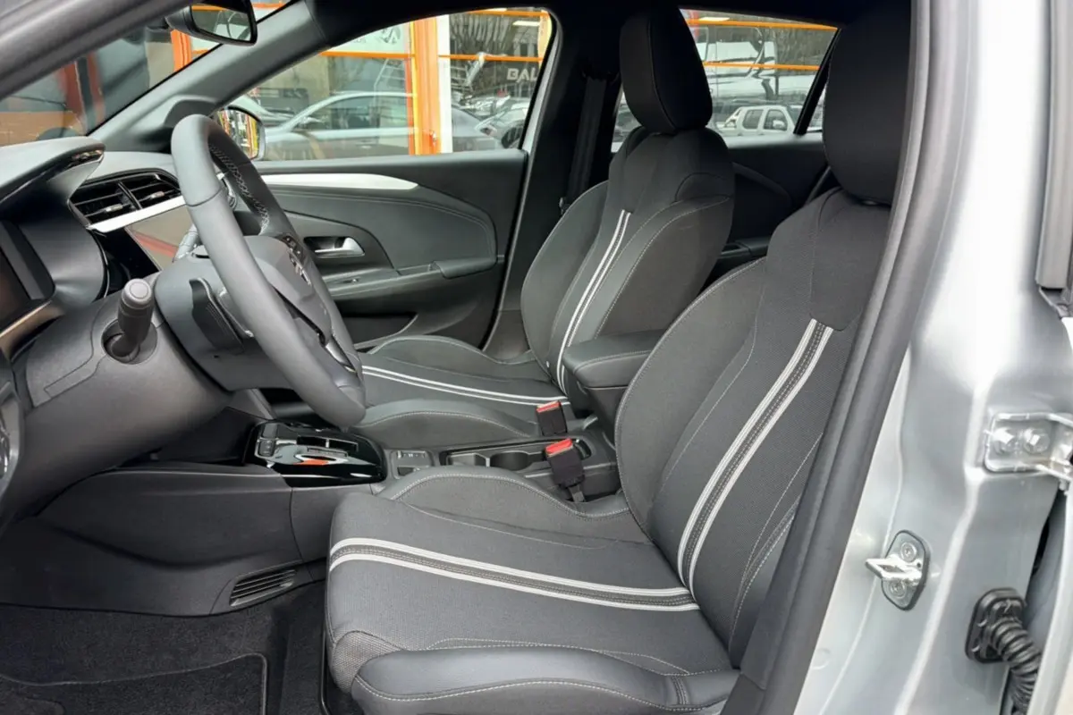 Vue intérieure côté conducteur de l’Opel Corsa gris kristall, sièges avant en tissu noir avec bandes blanches et volant multifonctions.