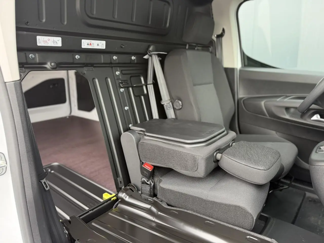 Vue intérieure côté droit du Citroën Berlingo blanc, mettant en valeur le siège passager rabattable et le plancher bois du coffre.