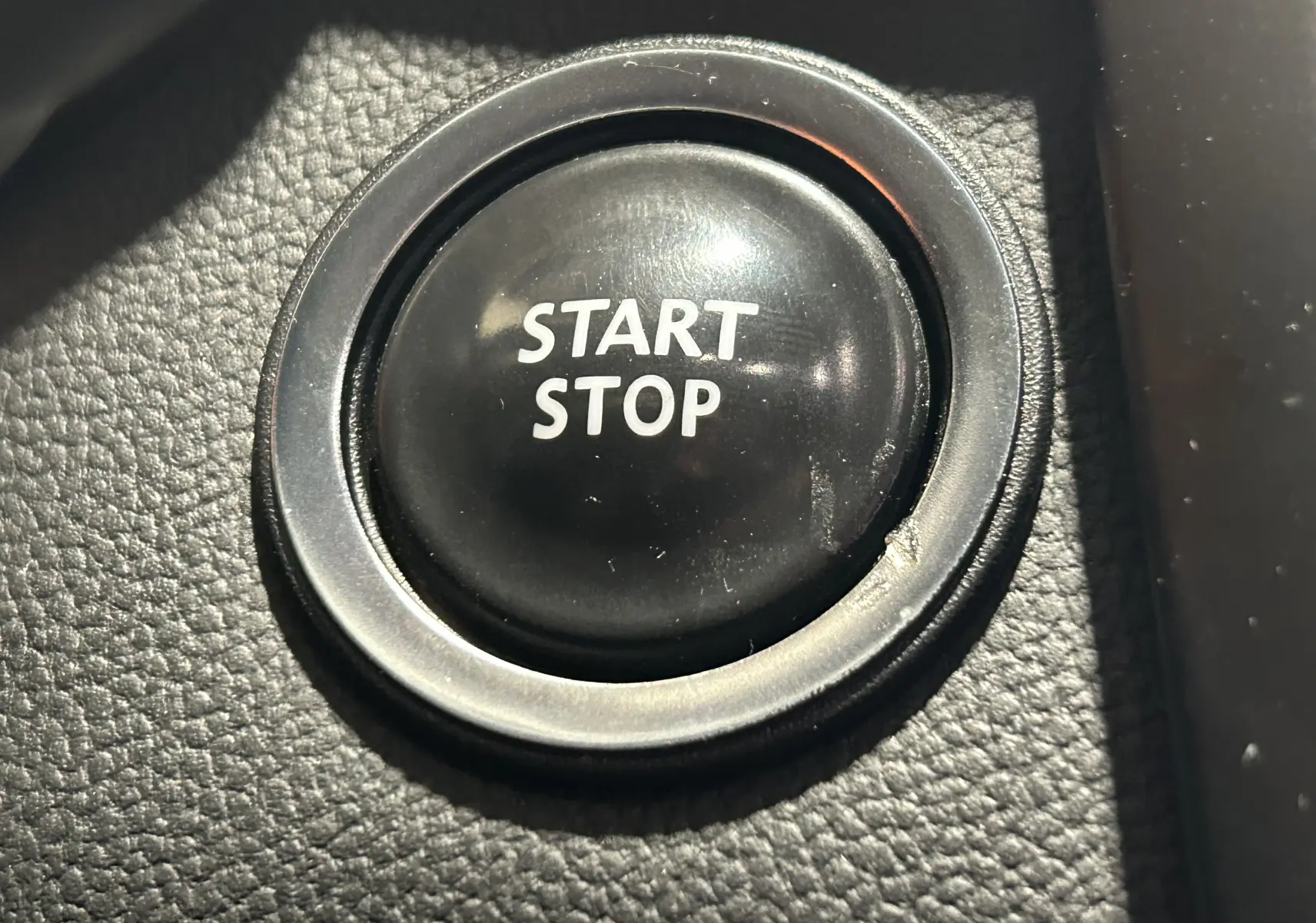 Bouton start-stop noir en gros plan sur le tableau de bord du Renault Kadjar gris diesel de 2015.