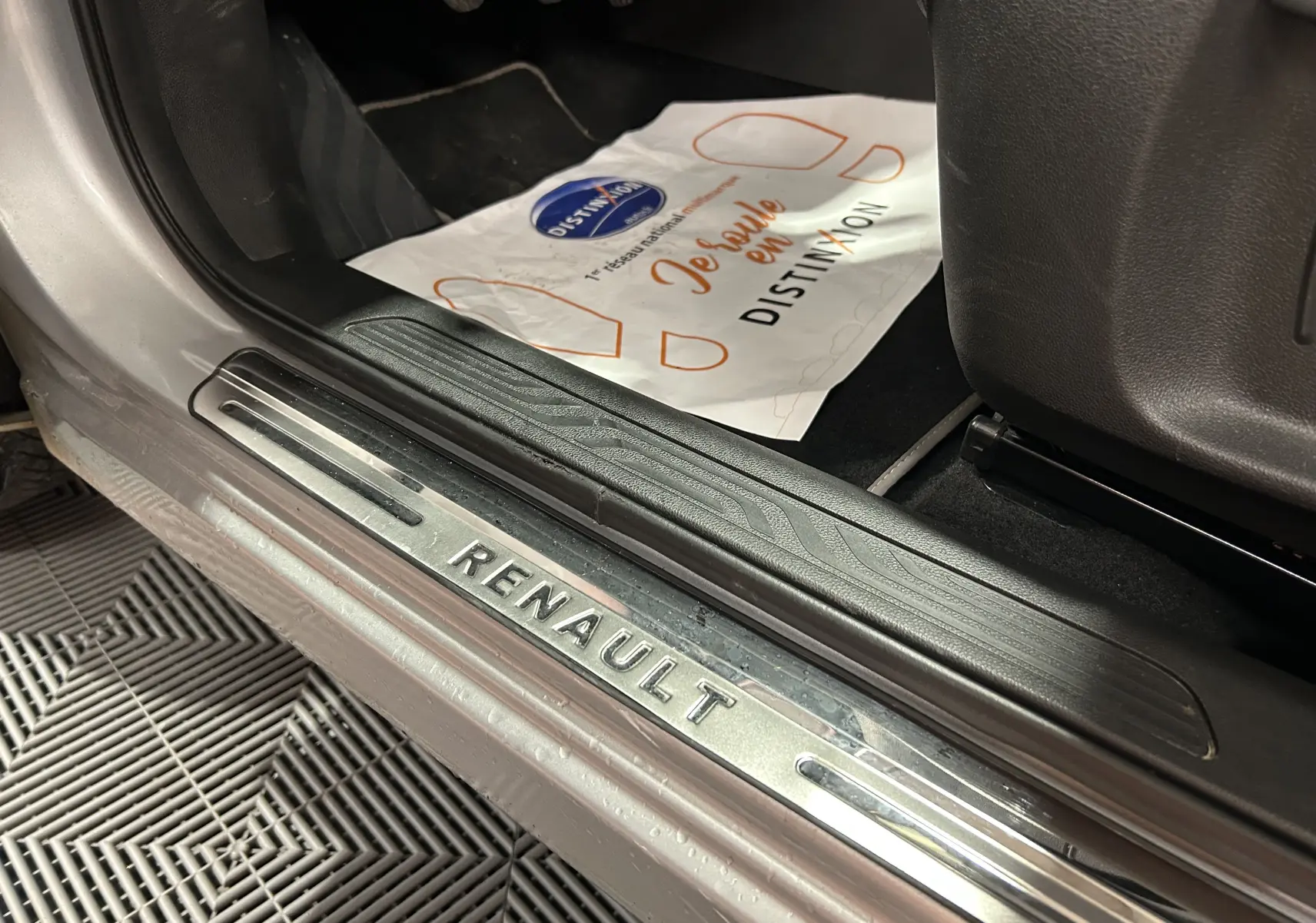 Gros plan sur la plaque de seuil de porte Renault côté conducteur d'un Kadjar gris, intérieur avec tapis noir.