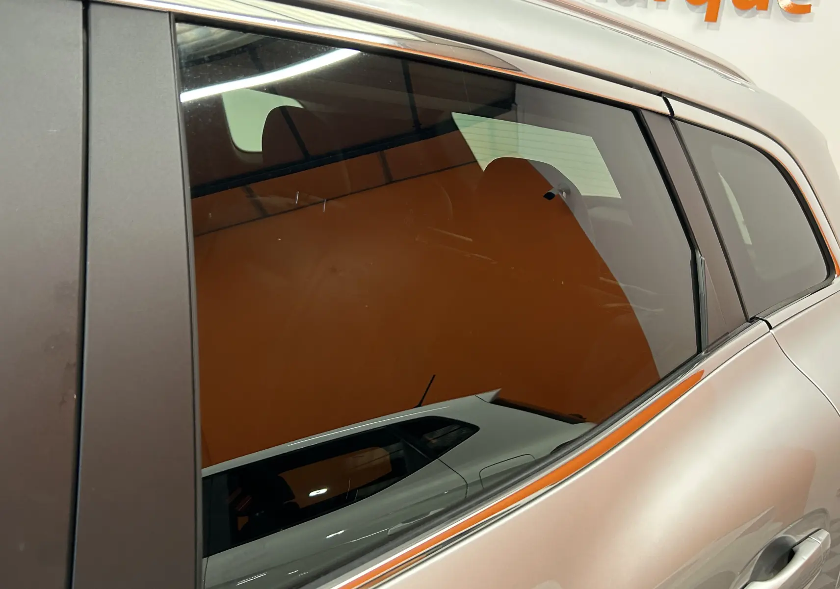 Reflet du profil côté gauche d'un Renault Kadjar gris 2015, mettant en valeur la ligne fluide et la vitre arrière teintée.