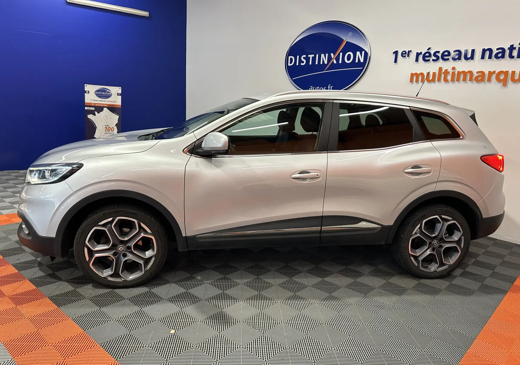 Profil côté gauche d'un Renault Kadjar gris 2015, SUV compact avec lignes fluides et vitres teintées, en intérieur showroom.