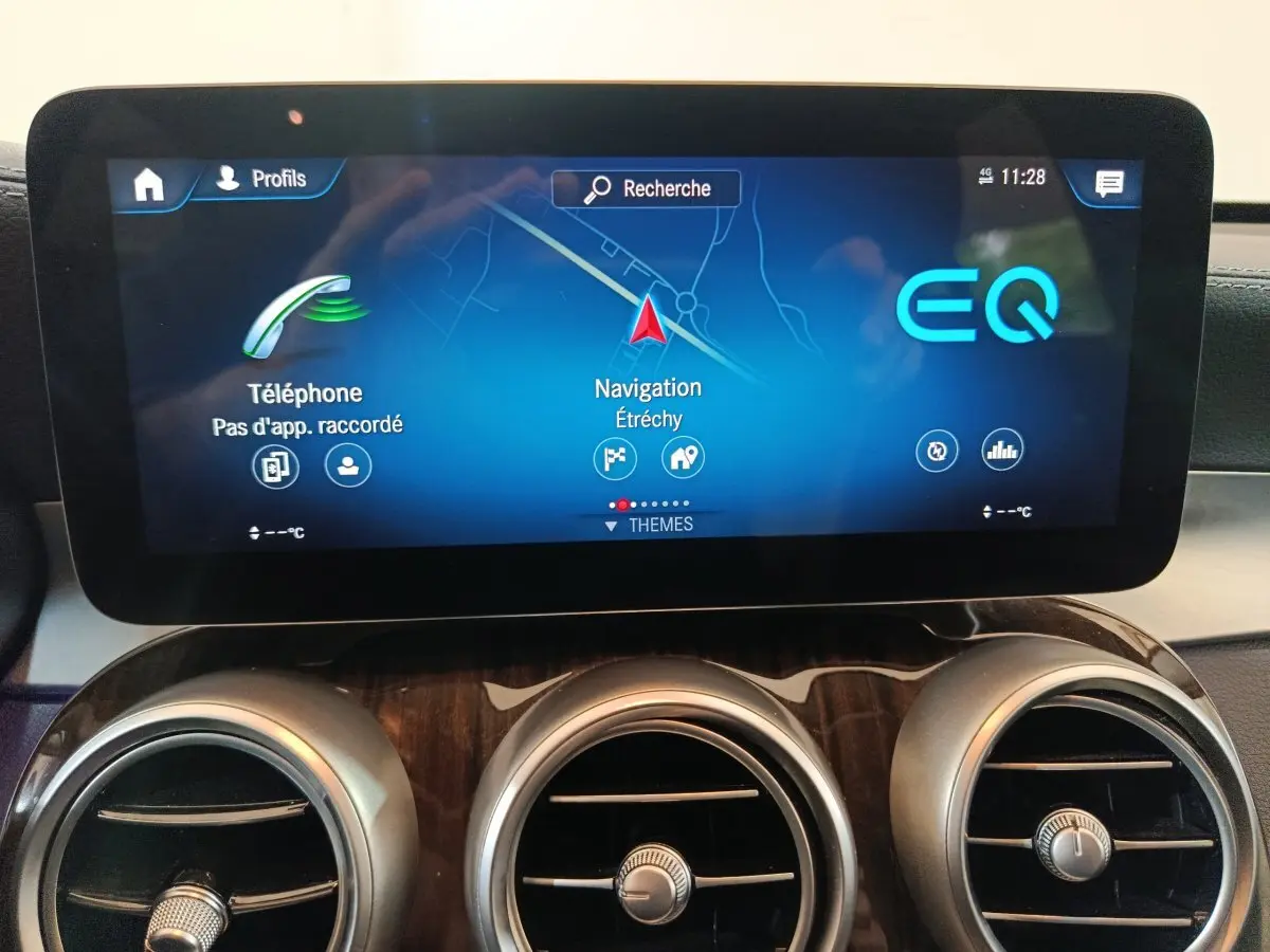Écran tactile central avec navigation et téléphone, tableau de bord bois et aérateurs ronds du Mercedes GLC 300 e noir.