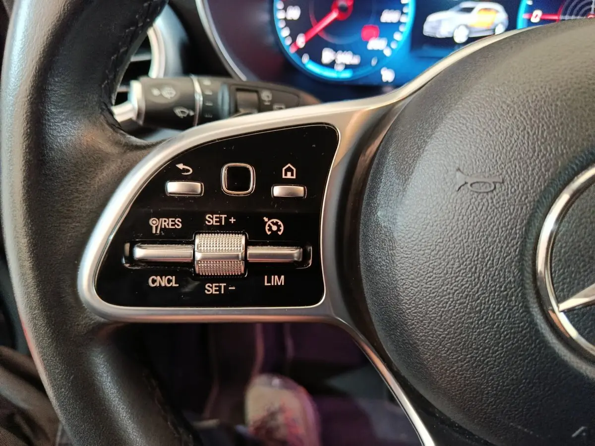 Gros plan sur le volant cuir noir du Mercedes GLC 300 e, avec commandes multifonctions et tableau de bord numérique.