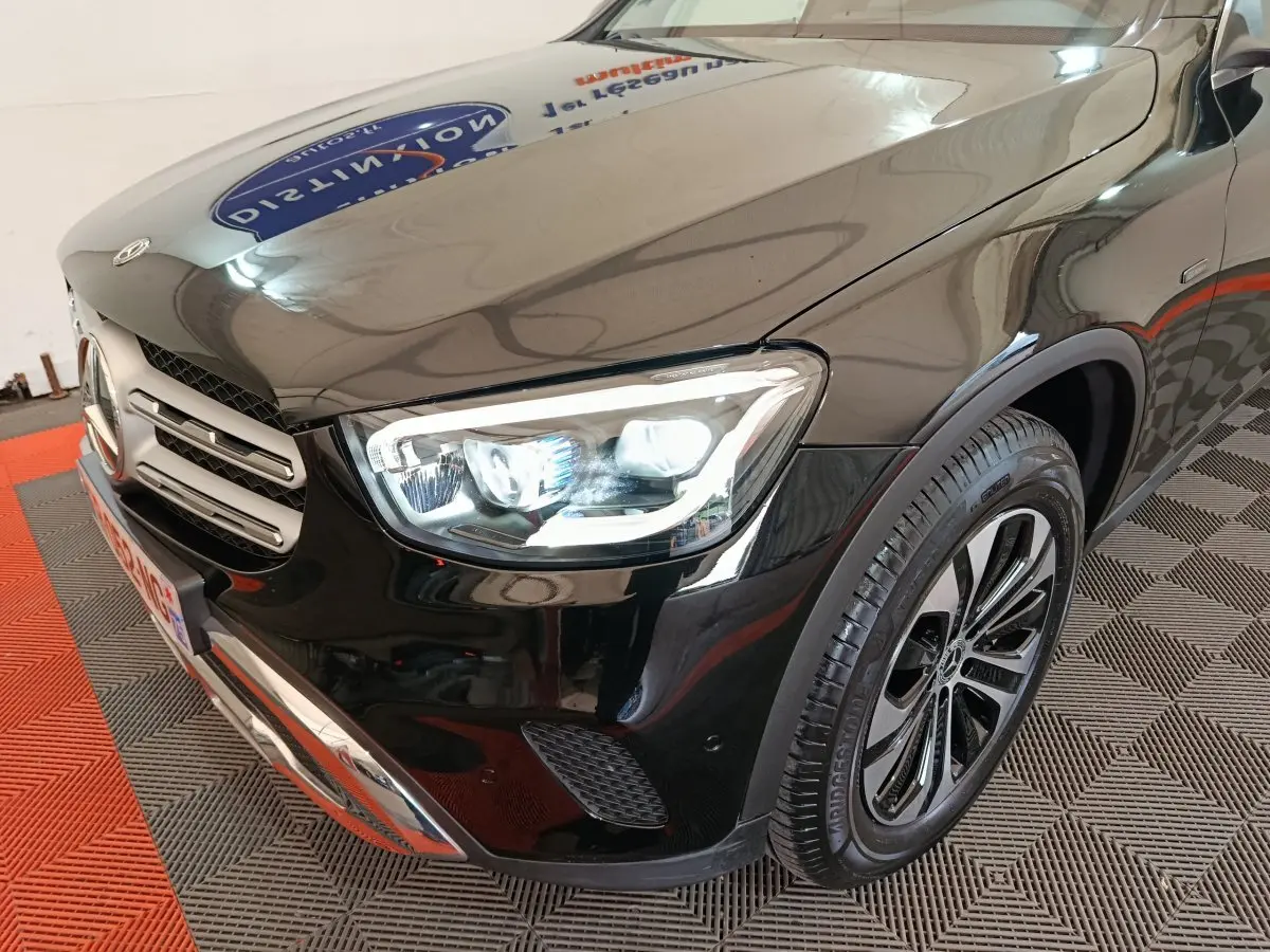Vue 3/4 avant droit d'un Mercedes GLC 300 e Business Line noir avec phares LED allumés et jante alliage distinctive.