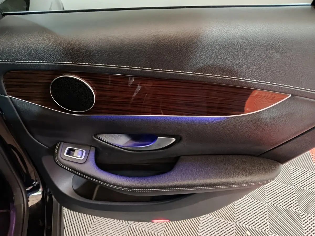 Gros plan sur la porte côté gauche du Mercedes GLC 300 e Business Line noir, avec insert bois et éclairage d'ambiance bleu.