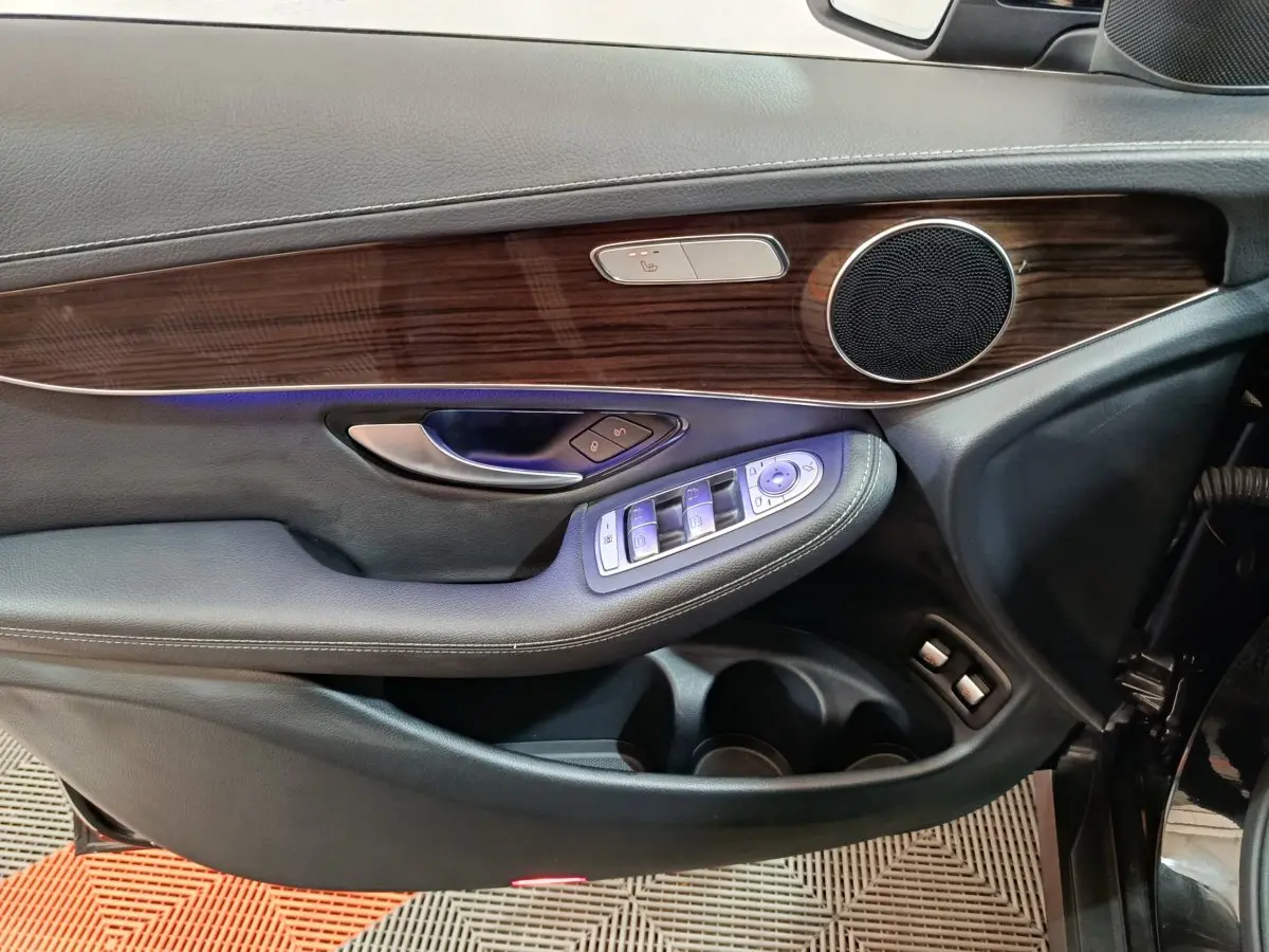 Gros plan sur la garniture en bois et les commandes électriques de la porte côté conducteur d'une Mercedes GLC noir.