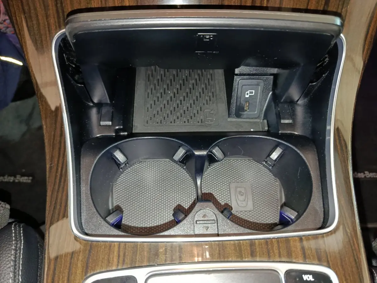 Gros plan sur les porte-gobelets et prise USB du coffre central en bois foncé d'un Mercedes GLC 300 e noir.