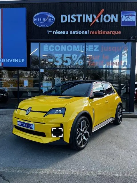 Renault R5 Techno jaune vue 3/4 avant droit, avec phares LED et jantes noires distinctives, devant un showroom multimarque.