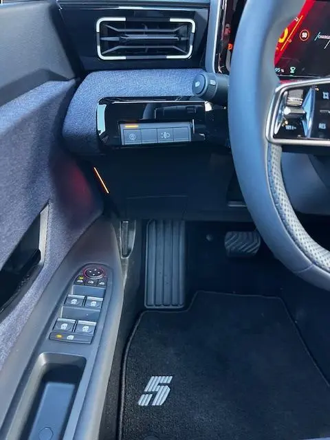 Vue intérieure côté conducteur de la Renault R5 jaune 2024, montrant les commandes de porte et le tapis noir avec logo "5".