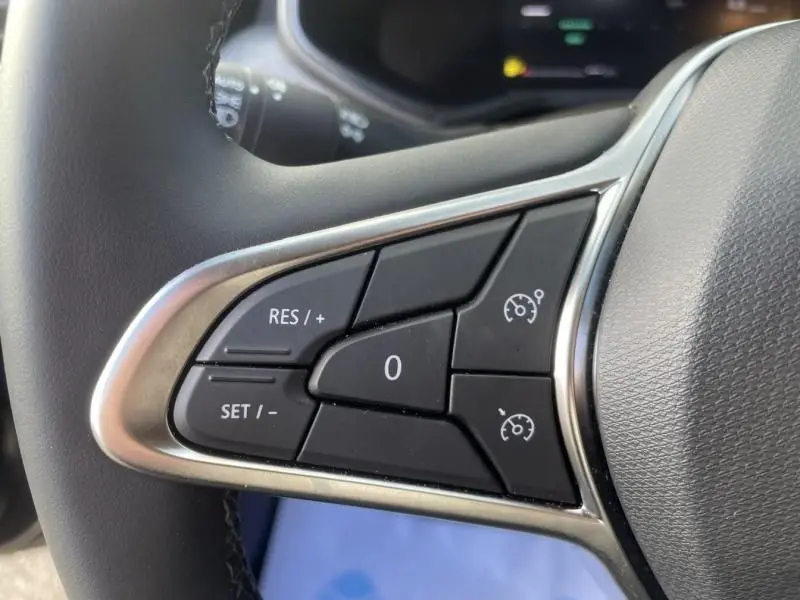 Gros plan sur les commandes au volant côté gauche de la Renault Clio V noire, avec régulateur de vitesse et finition chromée.