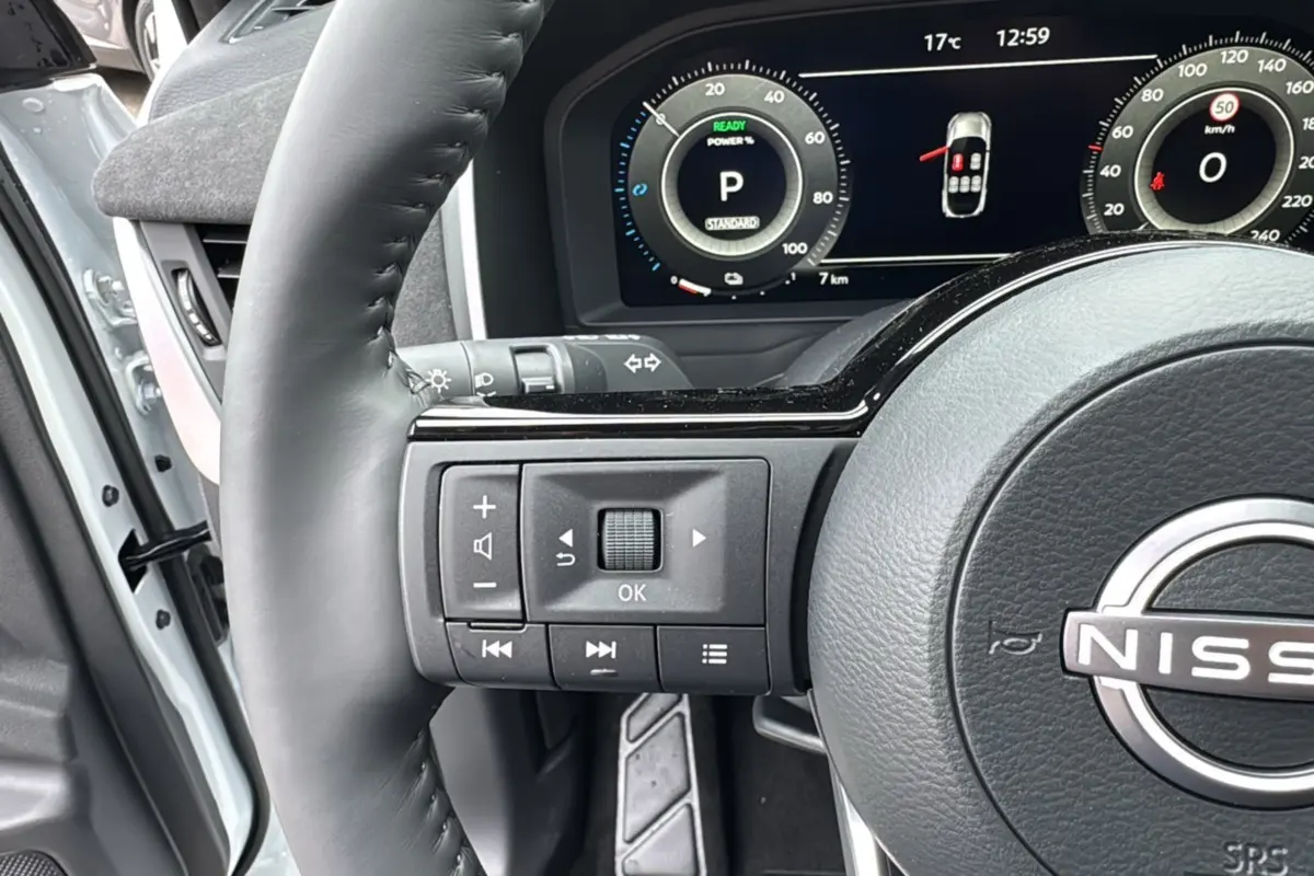 Gros plan sur le volant cuir noir du Nissan Qashqai E-POWER 205 Tekna Plus avec commandes multifonctions et tableau de bord digital.