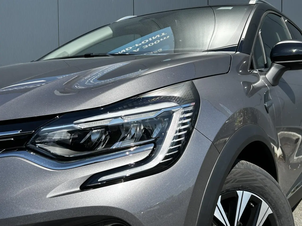 Gros plan sur le phare avant droit du Renault Captur 2024 gris Cassiopée avec jante alliage et rétroviseur noir étoilé.