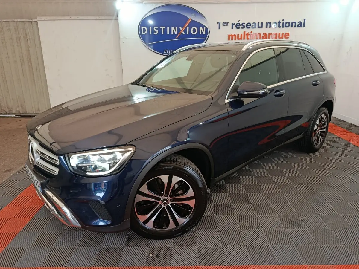 Mercedes GLC hybride rechargeable bleu en 3/4 avant droit, avec jantes alliage et phares LED allumés.