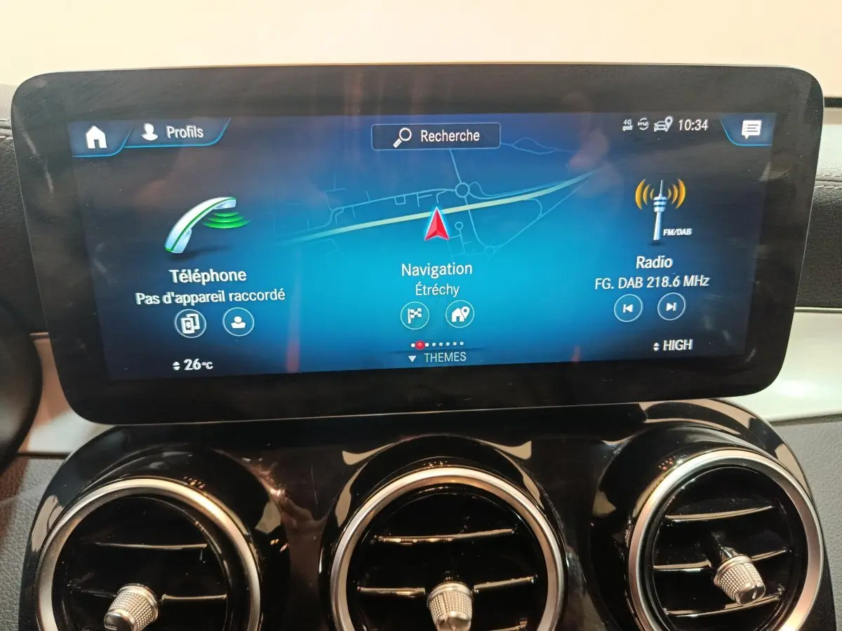 Écran tactile central affichant navigation et radio, avec aérateurs ronds chromés du tableau de bord d'une Mercedes GLC 300 E bleu.