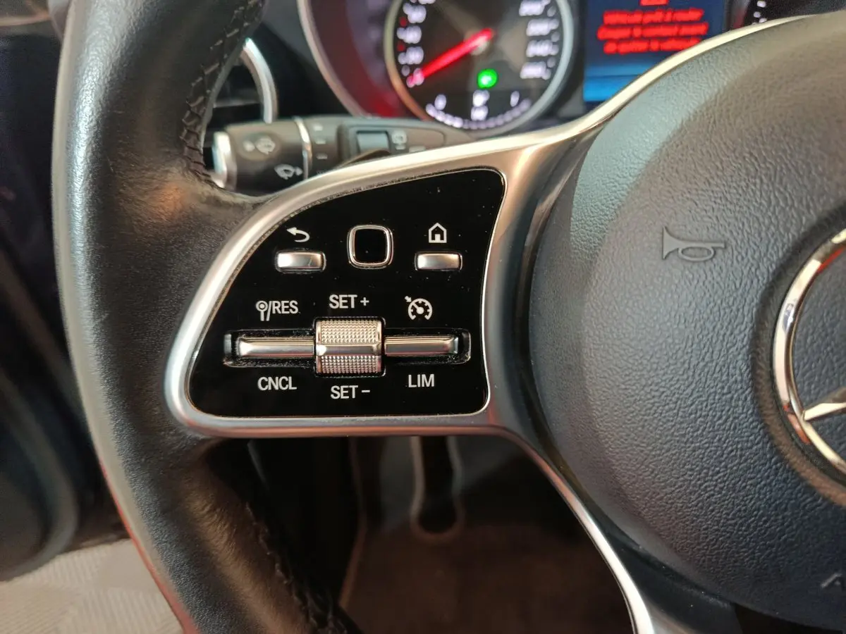 Gros plan sur les commandes du volant côté gauche d'un Mercedes GLC 300 E bleu, avec tableau de bord en arrière-plan.