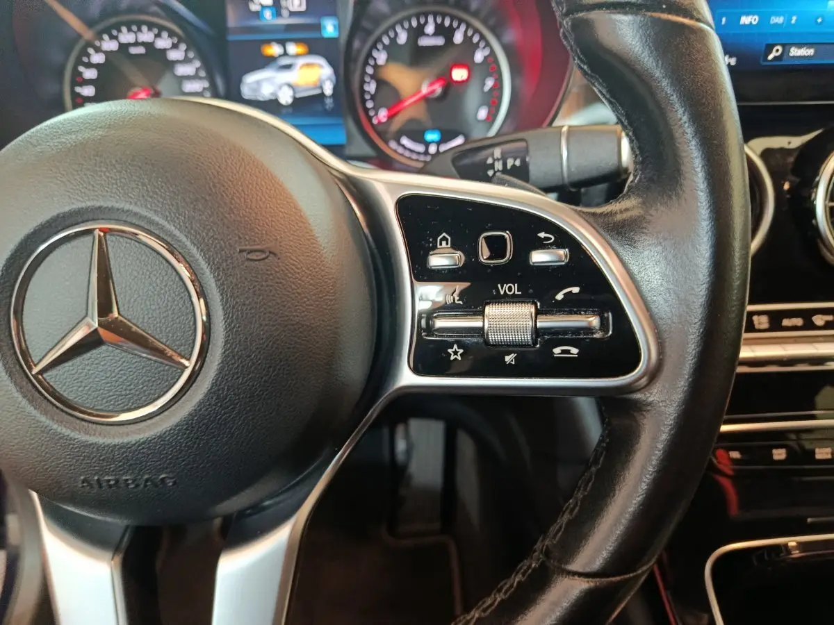 Gros plan sur le volant cuir noir de la Mercedes GLC 300 E Business Line 2021 avec commandes audio et tableau de bord lumineux.