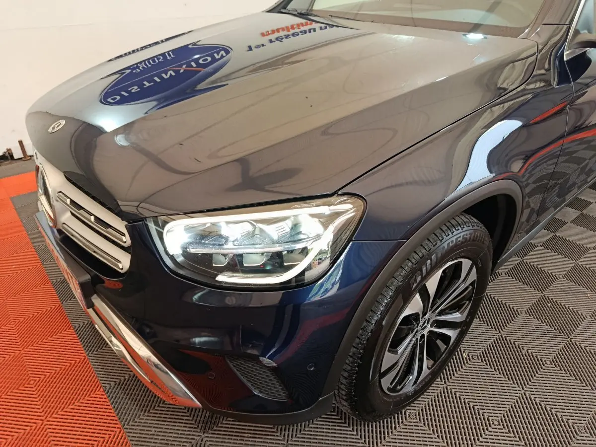 Vue 3/4 avant droit d'un Mercedes GLC 300 E Business Line bleu avec phares LED allumés et jantes alliage.