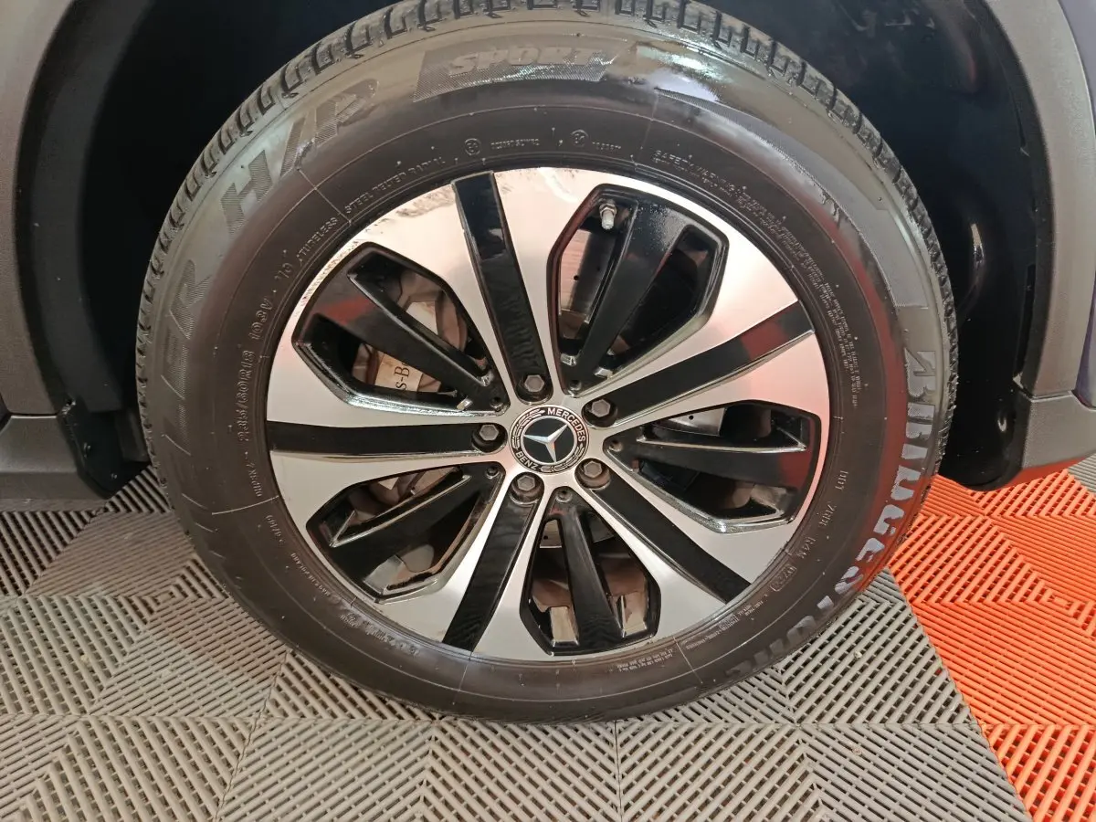 Gros plan sur la jante alliage bicolore noire et argentée d'un Mercedes GLC bleu, avec pneu Bridgestone visible.