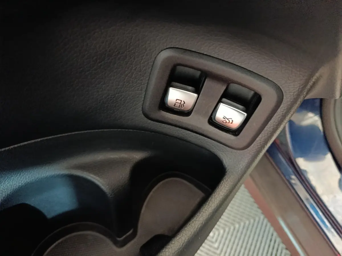 Gros plan sur les boutons d’ouverture du coffre et de la trappe à carburant, intérieur noir du Mercedes GLC bleu.