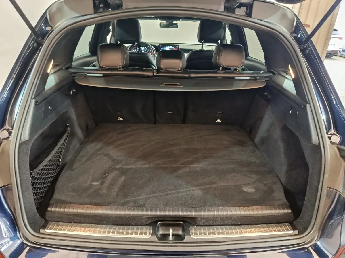 Coffre ouvert vu de l'arrière du Mercedes GLC 300 E Business Line bleu, avec cache-bagages et sièges noirs visibles.