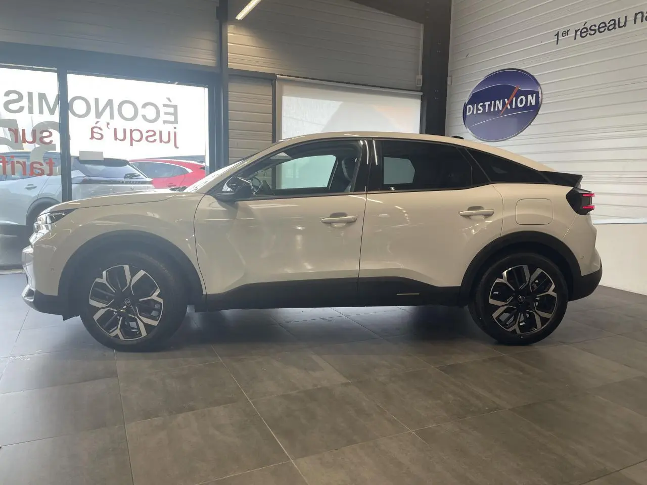 Profil droit d'une Citroën C4 blanche métallisée 2025 en showroom, avec jantes alliage et bas de caisse noirs.