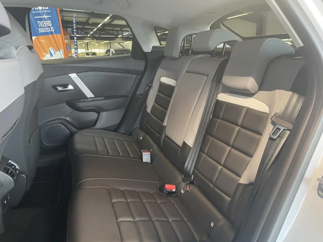 Vue latérale droite de la banquette arrière bicolore noire et beige de la Citroën C4 hybride 2025, avec ceintures et appuie-têtes.