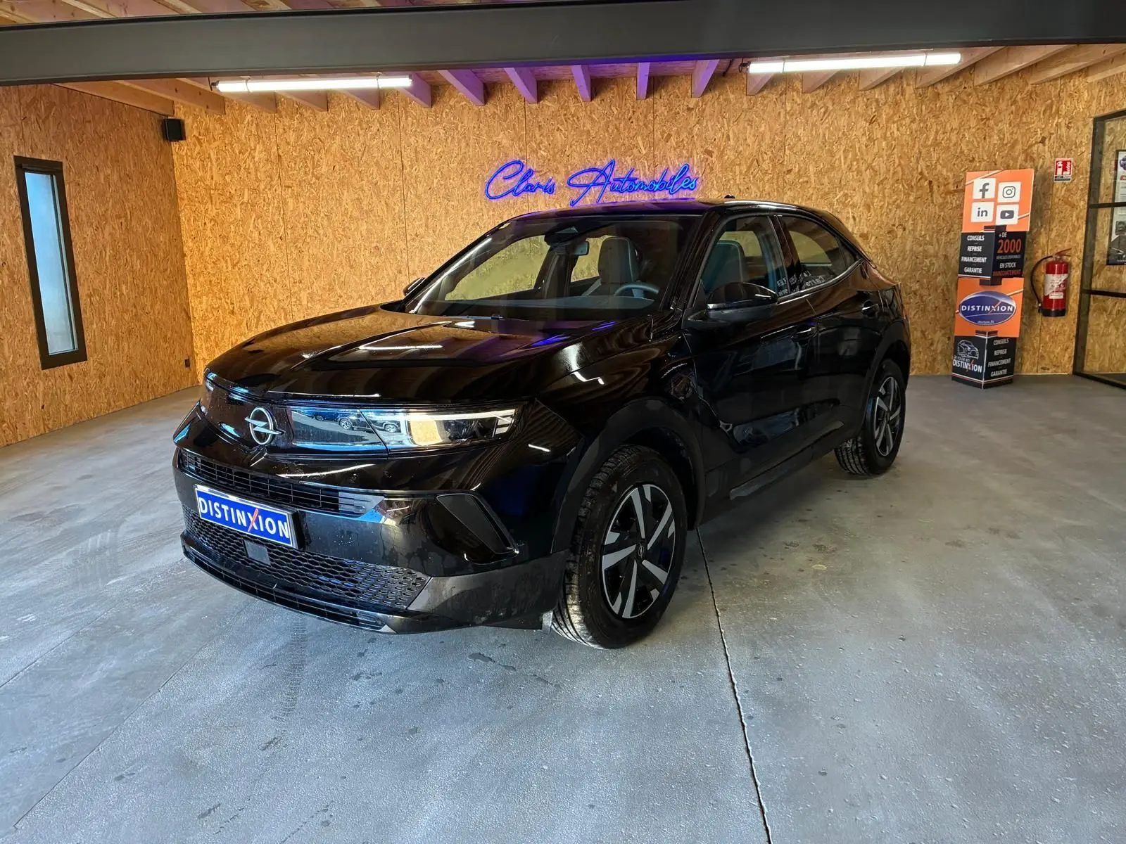 Opel Mokka 1.2 Turbo 145 Edition noir, vue 3/4 avant droit en intérieur avec éclairage naturel et néon bleu.
