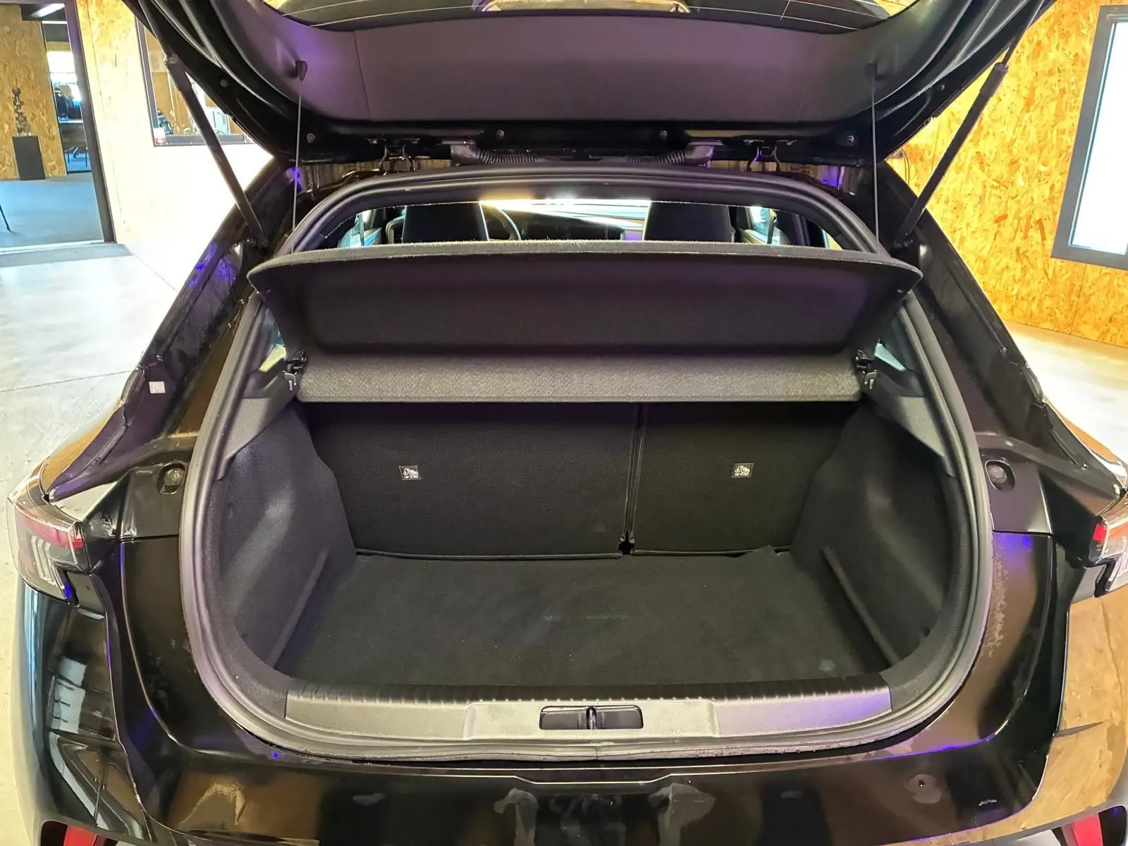 Coffre ouvert vu de l'arrière d'un Opel Mokka noir 2025, montrant l'espace de chargement vide et la tablette cache-bagages.