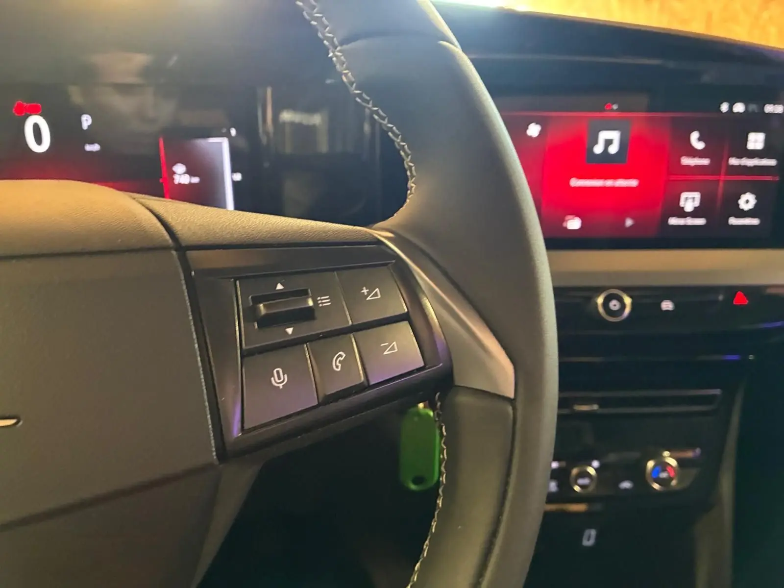 Vue intérieure du tableau de bord et volant noir de l'Opel Mokka 2025, avec commandes audio et écran tactile rouge en arrière-plan.