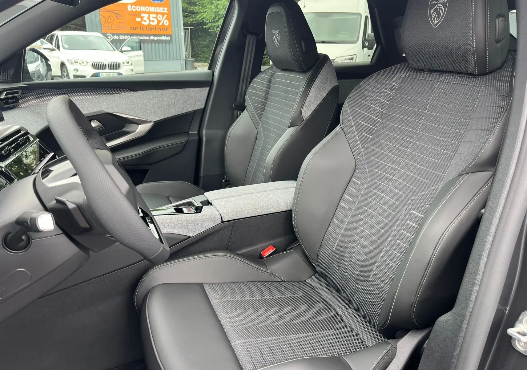 Vue intérieure côté conducteur du Peugeot 3008 gris titane 2025, sièges tissu et cuir avec logo Peugeot brodé sur appuie-tête.