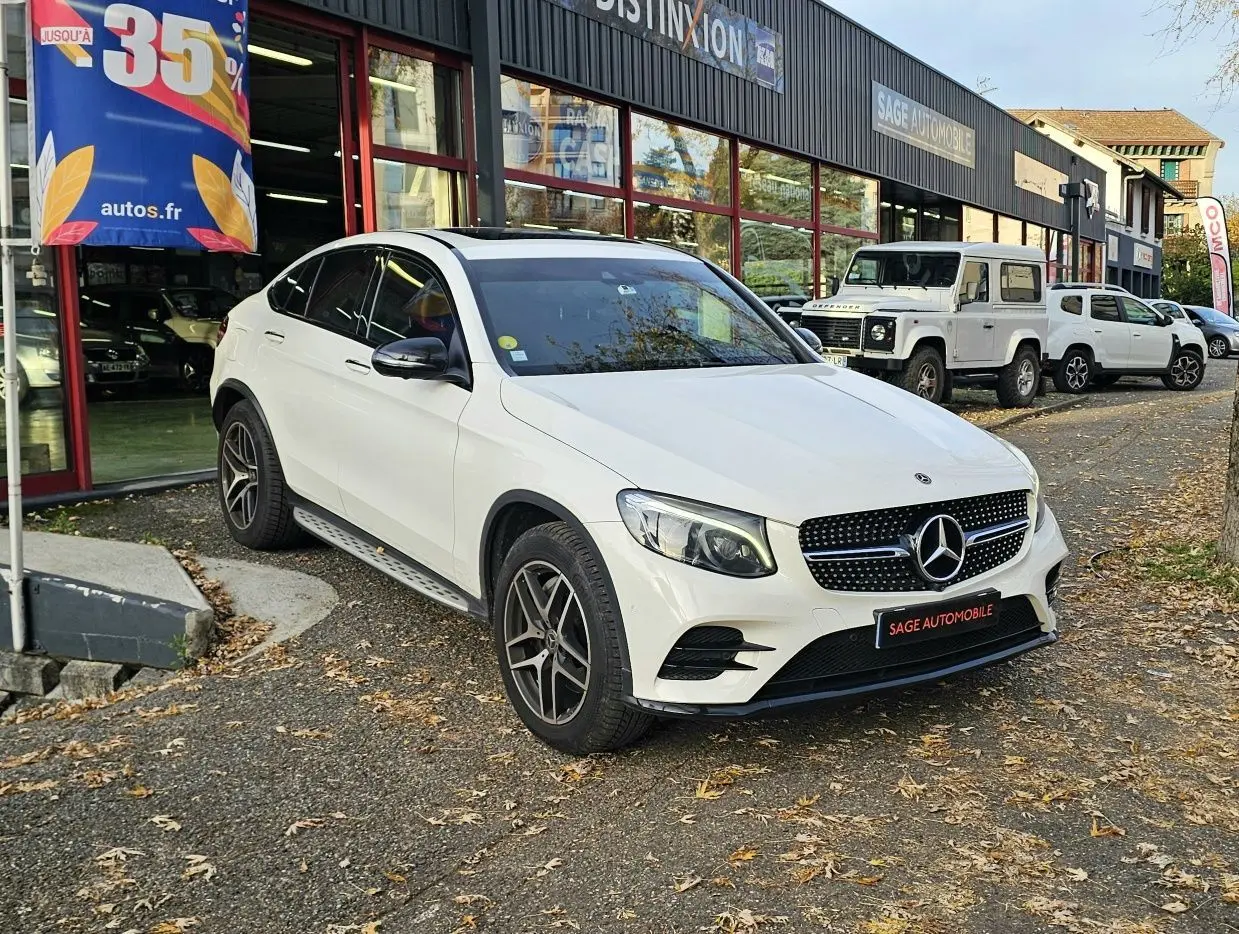 Mercedes GLC 220 Coupé blanc en 3/4 avant droit, avec calandre diamant et jantes alliage foncé, stationné devant un garage.