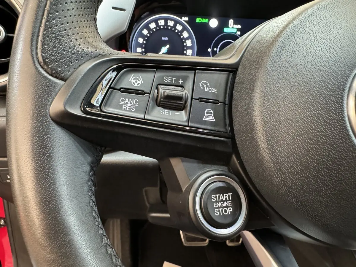 Gros plan sur le volant cuir noir de l'Alfa Romeo Tonale rouge 2023 avec commandes de régulateur et bouton start/stop visible.