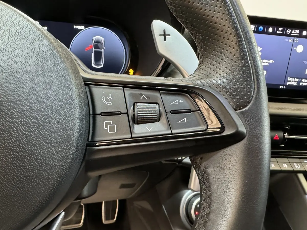 Gros plan sur la partie gauche du volant en cuir perforé de l'Alfa Romeo Tonale rouge avec commandes multifonctions et palettes de vitesse.