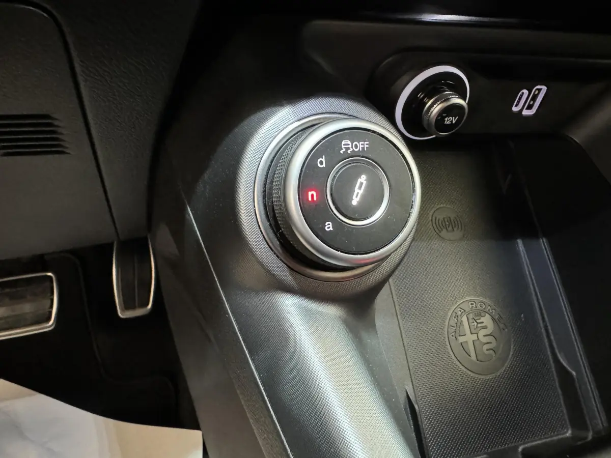 Gros plan sur la molette de sélection de boîte auto et la zone de recharge avec logo Alfa Romeo dans l'habitacle noir du Tonale.