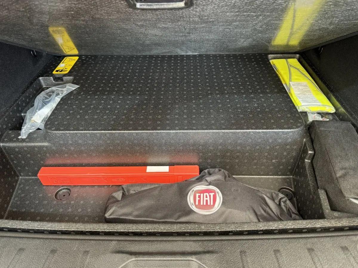 Compartiment de coffre ouvert montrant un kit de sécurité noir avec logo Fiat et un triangle de signalisation rouge.