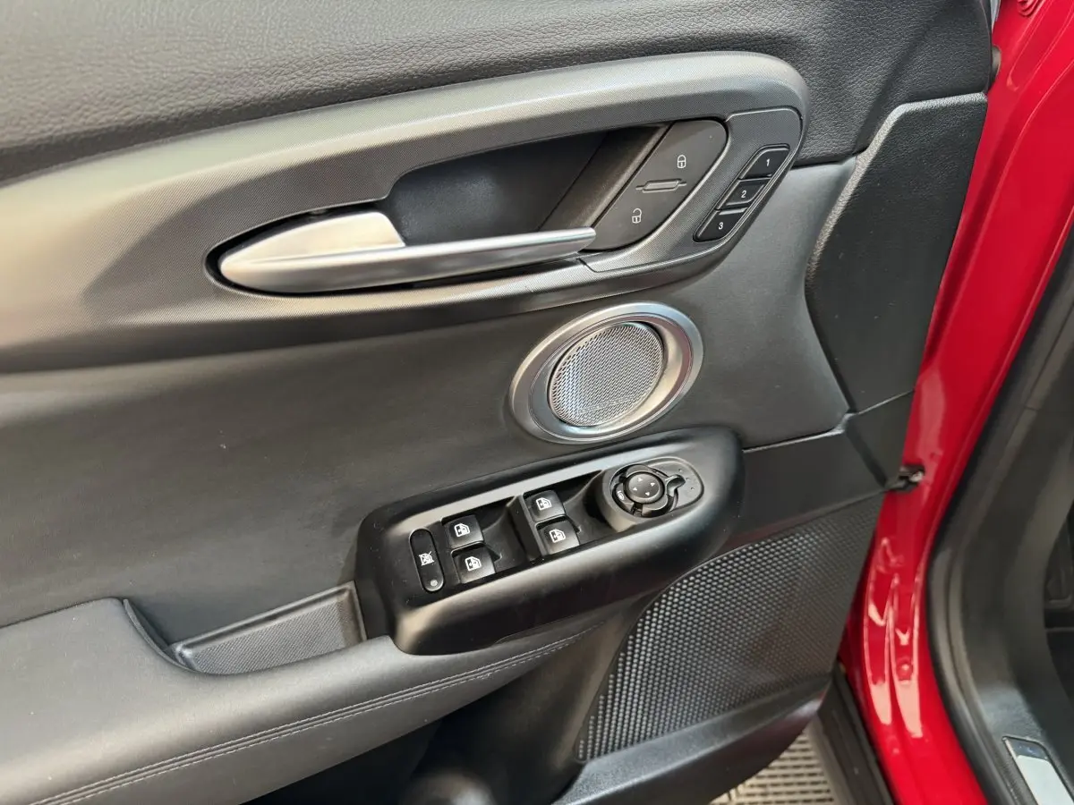 Gros plan sur la porte avant gauche rouge de l'Alfa Romeo Tonale avec commandes de vitres et haut-parleur intégré.